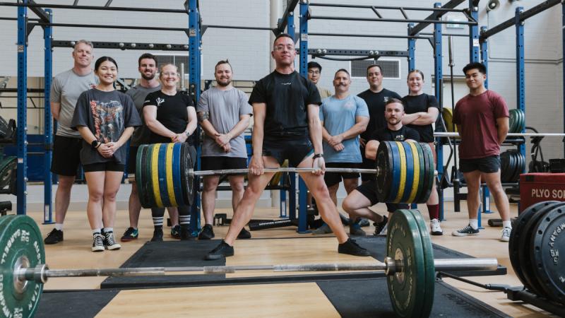 An Air Force powerlifter demonstrates a deadlift to teammates in a gym.  