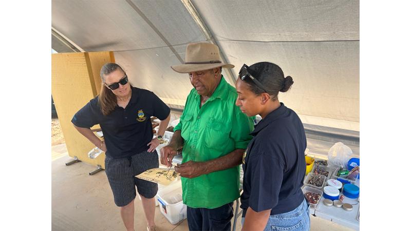 A man and two women discuss a piece of text in the man's hands.