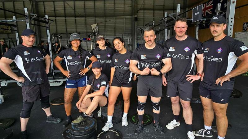 A team of powerlifters wearing black uniforms stands in a gym with gym equipment.