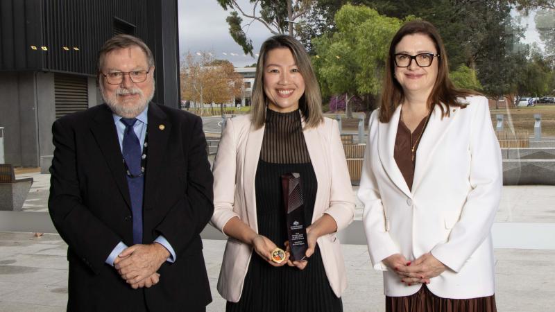 Two women and a man stand with an award.