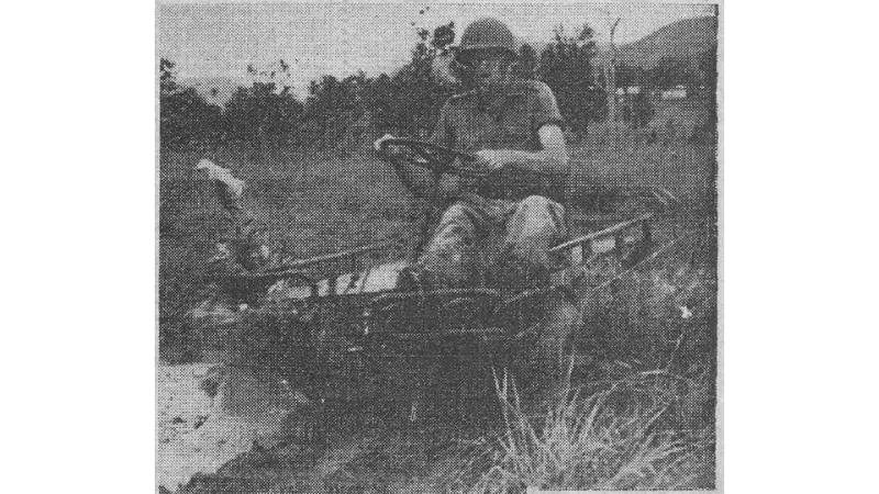 A grainy black and white newspaper photo shows a soldier seated on a small Mechanical Mule, holding the steering wheel with both hands.
