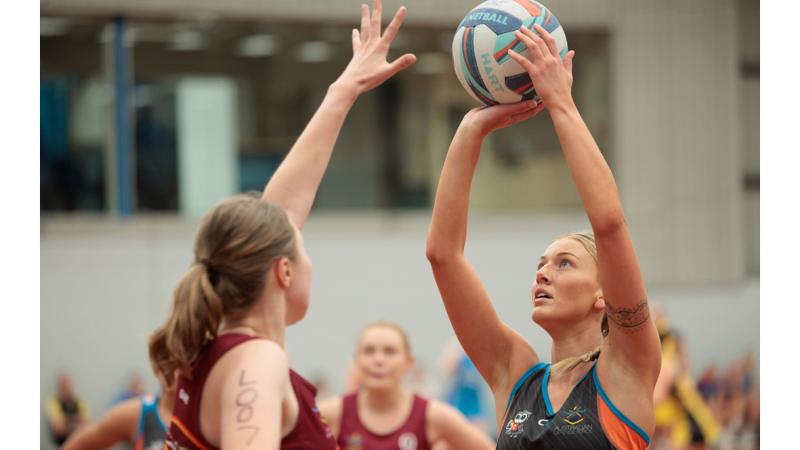 A women shoots for goal during a netball game.