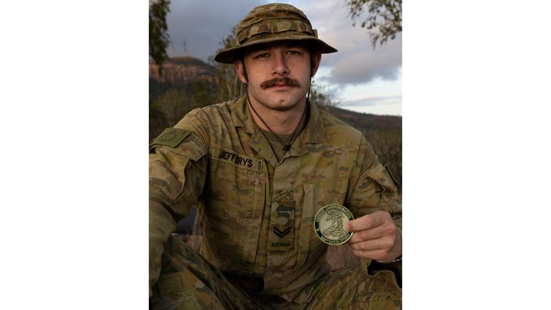 An Army soldier holding up a medal. 