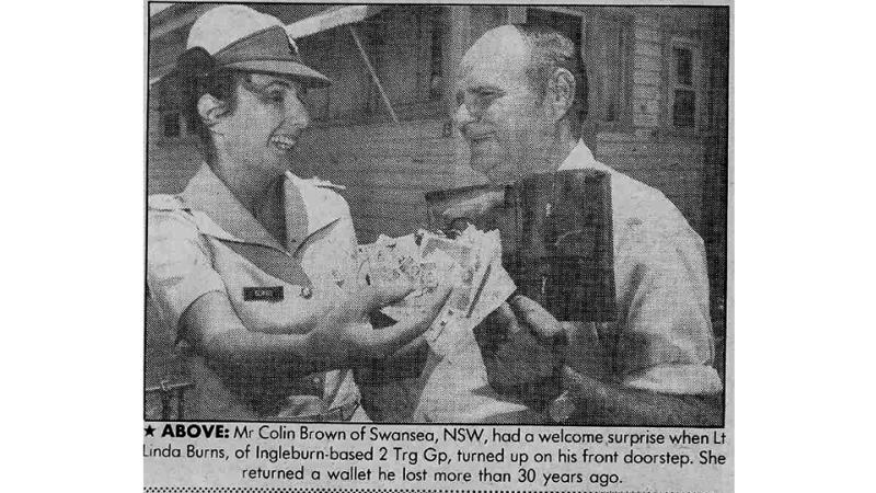 A grainy black and white newspaper photo with caption showing a man holding a wallet and the soldier holding its contents, both smiling.