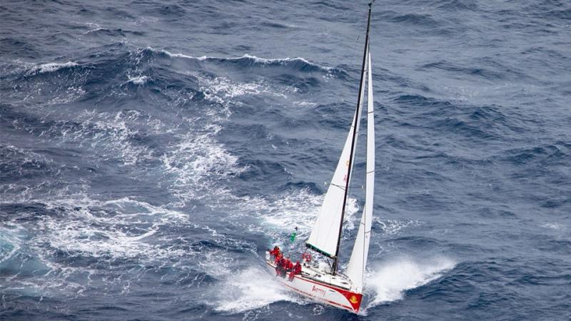 Several people in red uniforms on a red and white yacht with the word Army on its side sailing in open water.