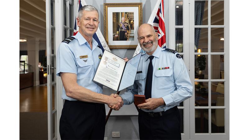 Two military personnel shake hands and display an award.