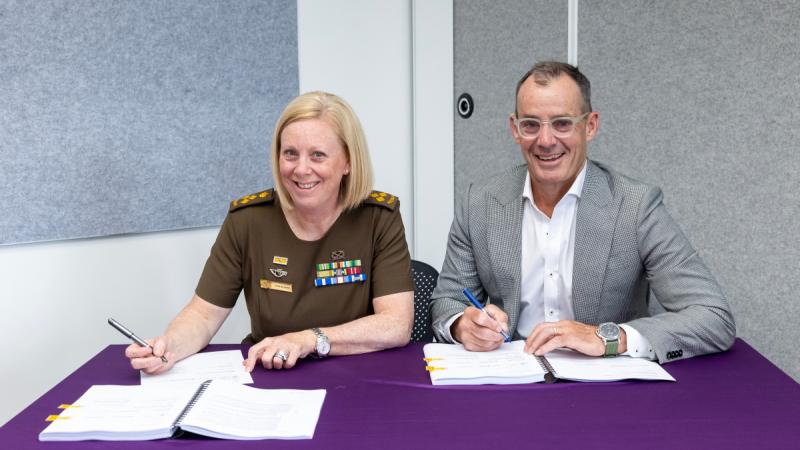 Two people, one in uniform and one in a suit, sitting at a desk signing documents.