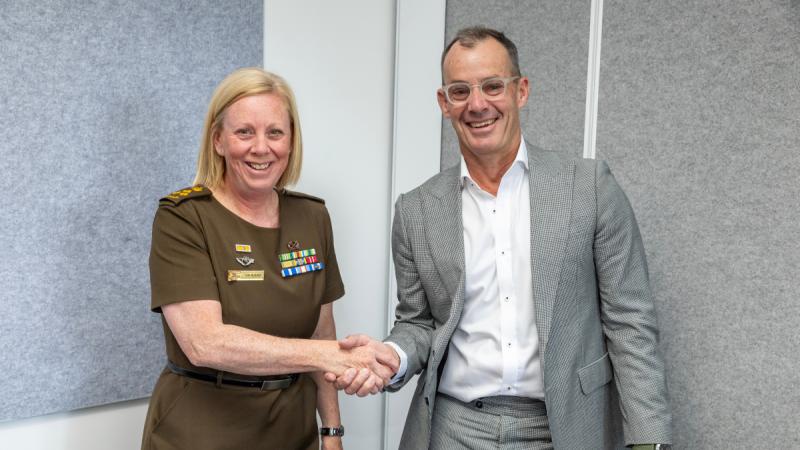 Two people, one in uniform and one in a suit, standing and shaking hands in an office.