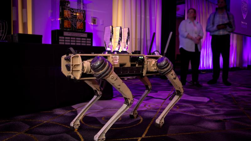 A robotic dog on a stage with three glass trophies on its back.