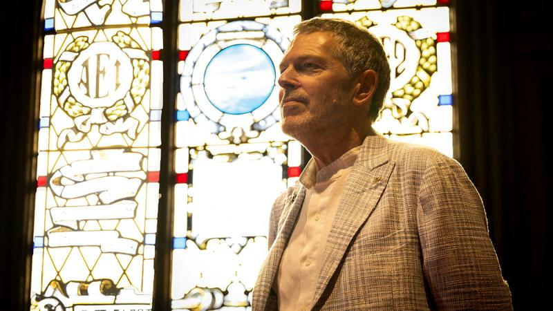 A man stands in front of a stained glass window as light filters in.