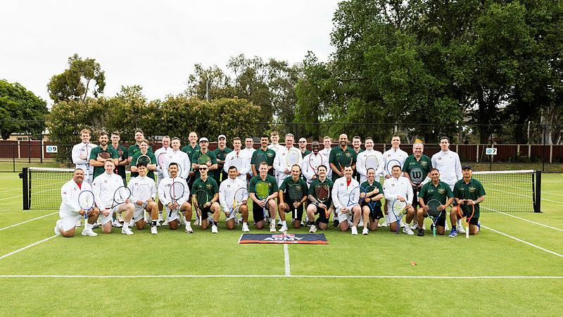 Two tennis teams - ADF and the British Army team - pose for a photo on a grass tennis court.