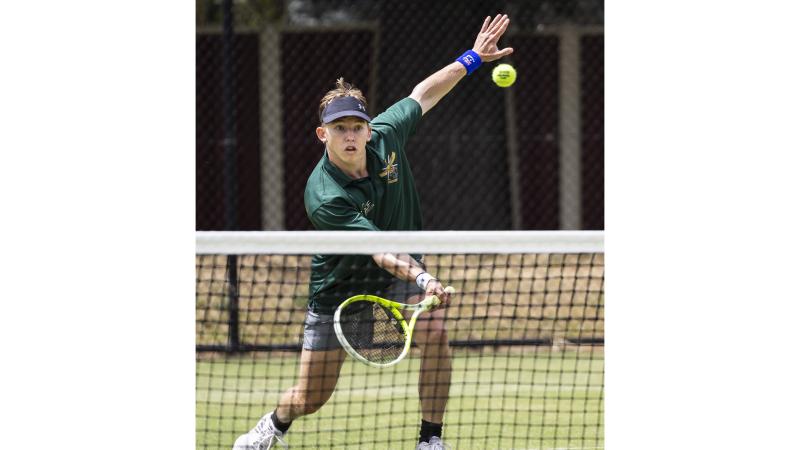 A tennis player is seen from the other side of the net about to hit the ball.