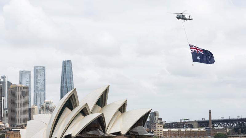 A Navy MH-60R helicopter displays the Australian National Flag over Sydney Harbour for Australia Day.