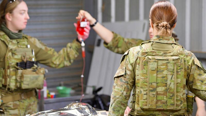 An Army member supports a bag of blood held by another as a mock casualty receives treatment for a wound.