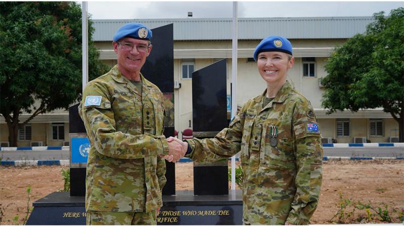 Two military personnel shake hands in front of a monument.