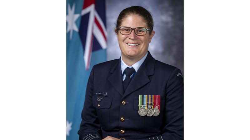 Group Captain Aleisha Broadhead poses for a portrait in her Air Force uniform with the Australian flag in the background.