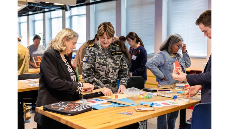 Civilians and a female military member work at a desk.