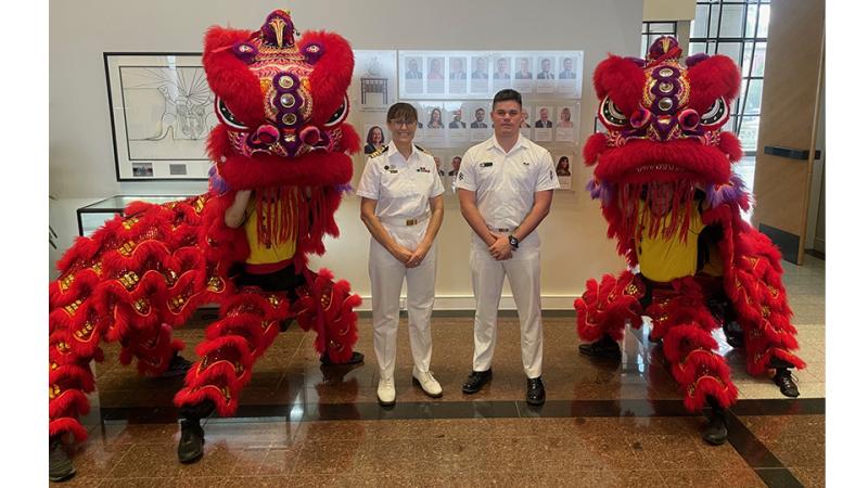Two military personnel stand with two Chinese dragon dancers.
