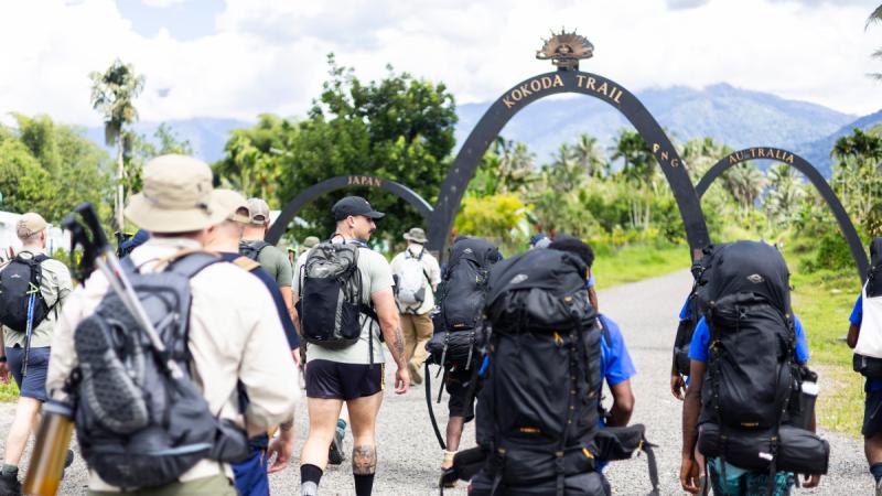 People wearing backpacks walking toward an arch marked Kokoda Trail.