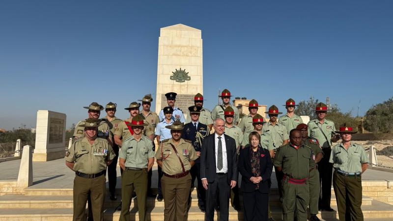 A group of people, most in military uniform, standing on steps in front of a stone memorial.