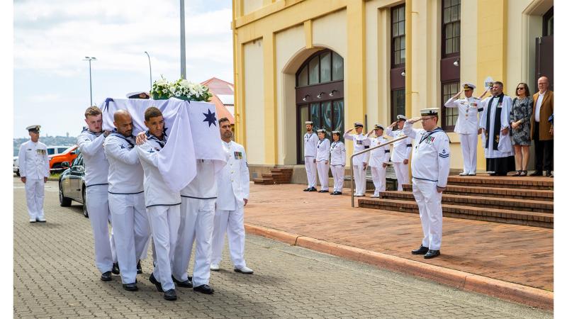Military personnel carry a coffin past a church.