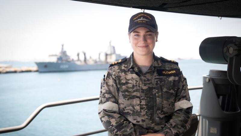 A sailor on the port bridge wing of a ship, with another ship visible in the distance.