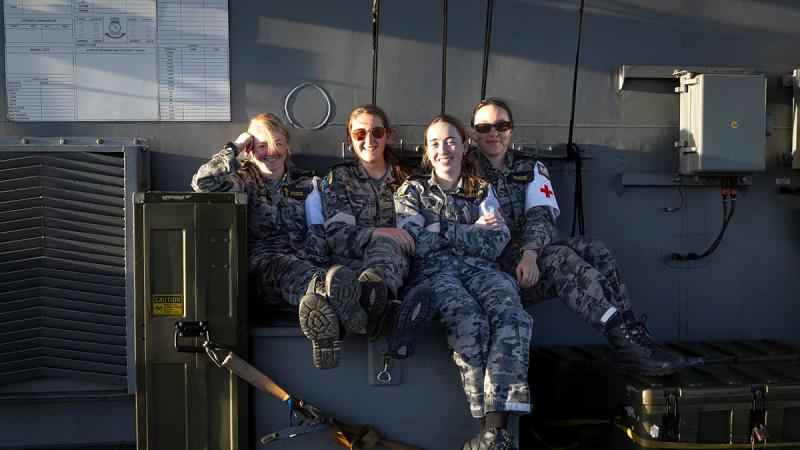 Four Navy medics, all wearing uniforms and crosses on their arms, sit together in a casual pose.