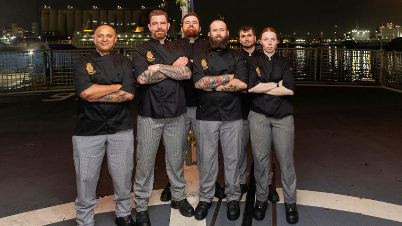 Navy personnel pose with arms crossed at night time.