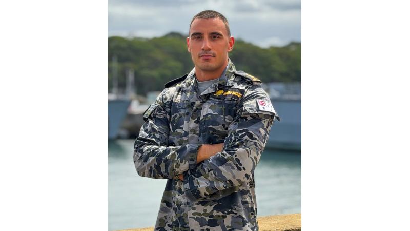A military member stands before several ships docked near shore.