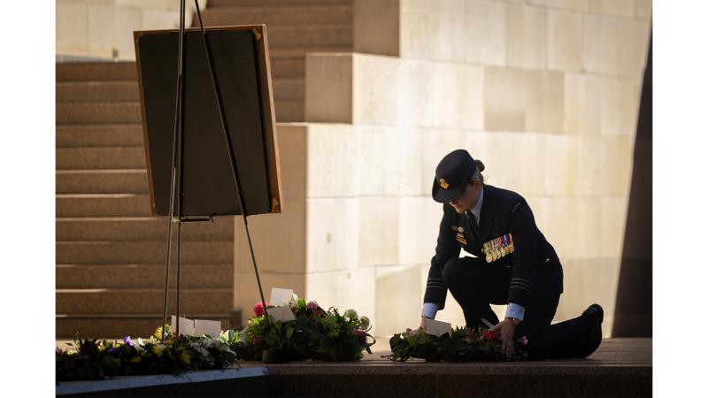 A military woman lays down a wreath before a framed photo.