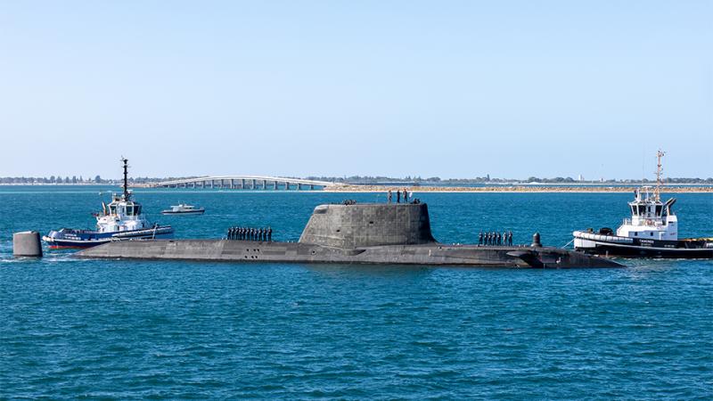 A submarine surfaces near a dock.