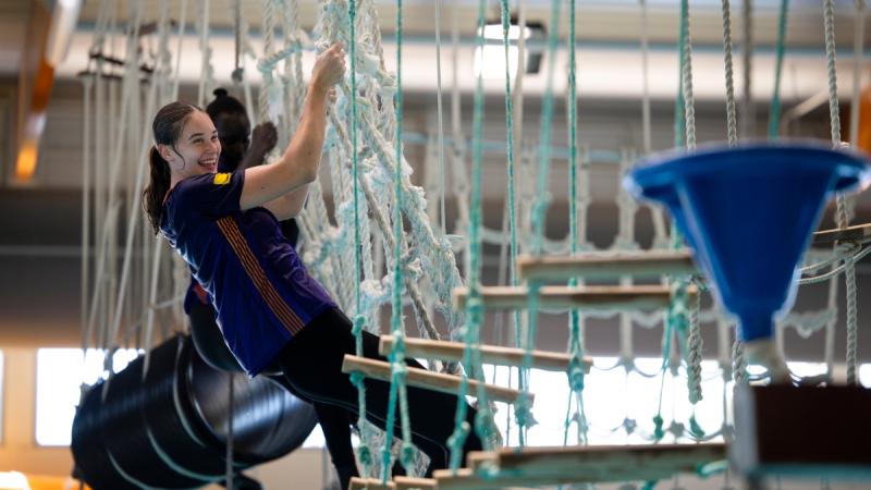 A woman smiles as she climbs a rope obstacle course.