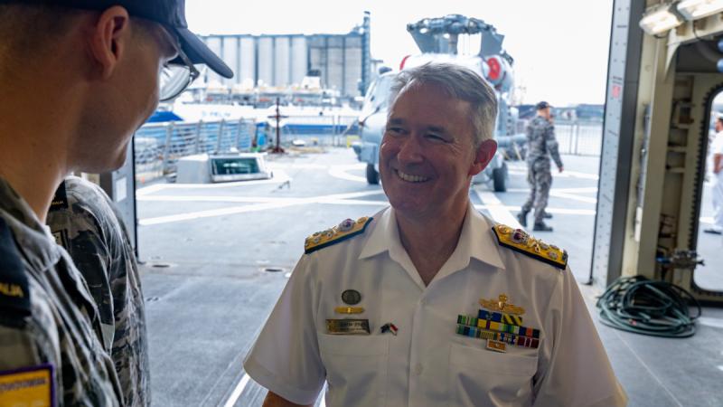 An officer smiles while talking with a sailor on a covered deck area.