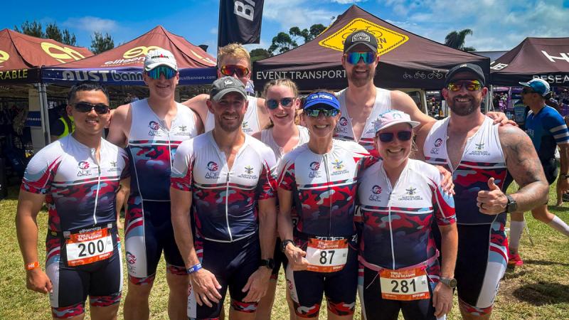 A group of people wearing matching ADF sportswear smiling and standing in front of portable gazebos.
