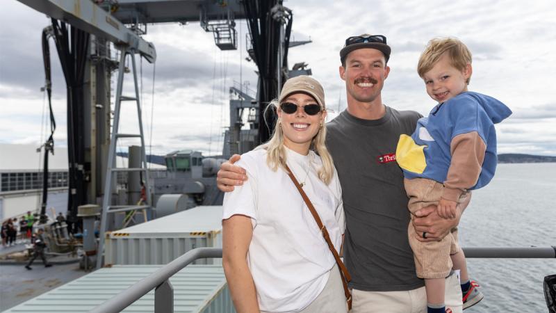 A young couple and child stand on board a ship.