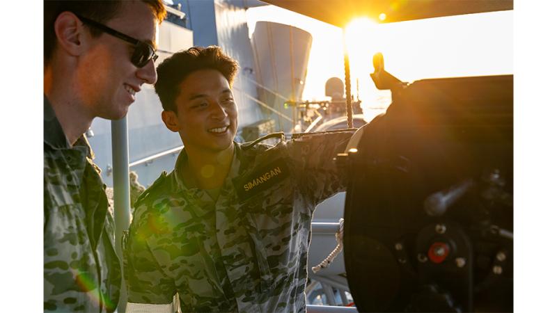 Two military personnel assess a piece of ship equipment.