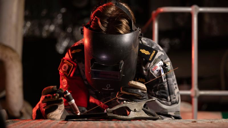 A person wearing a welding mask welds inside a ship.