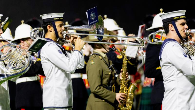 A man in Navy whites plays a trombone beside other members of a marching band.