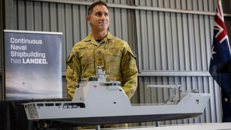 A man in Army uniform standing behind a model of a ship.