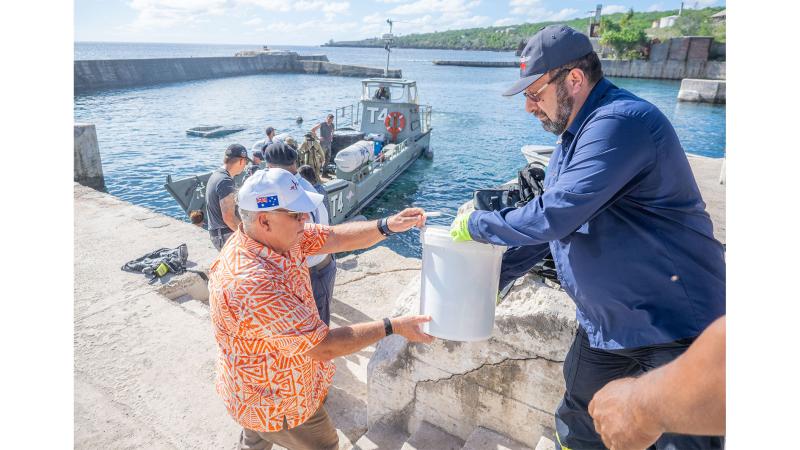 Two men exchange a bucket by a docked boat.
