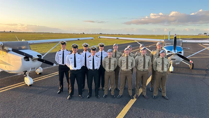 Military personnel stand near aircraft on the runway.