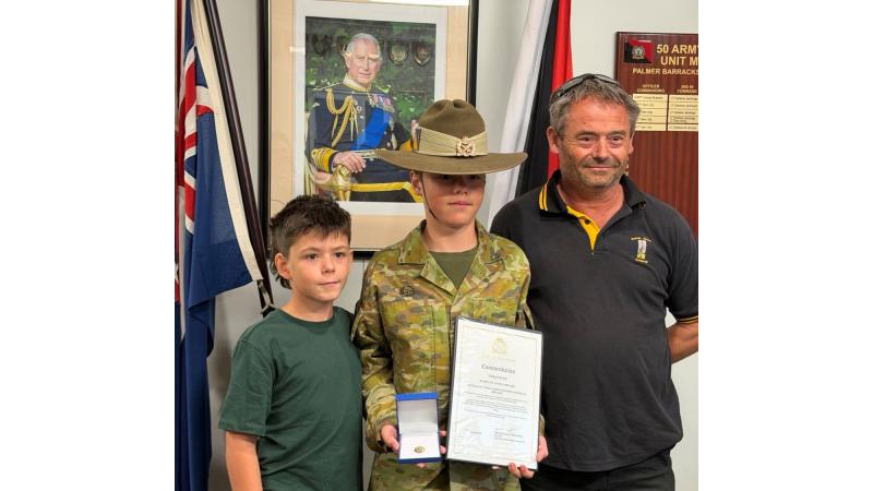 A young boy in Army uniform, flanked by his brother and father, holds an award and certificate.