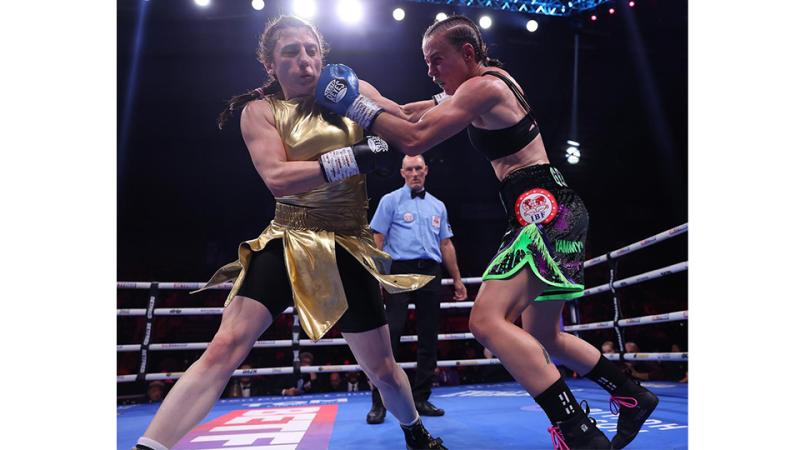 Two female athletes box in a ring with an umpire.