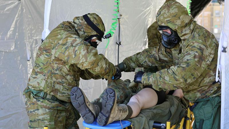 Two ADF personnel in protective gear work on a casualty on a raised table.