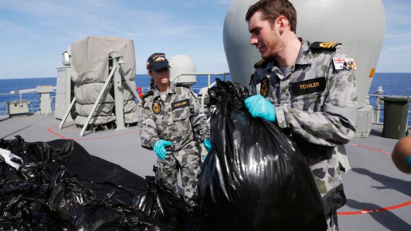 A man and a woman in Navy uniforms dispose of large black rubbish bags.