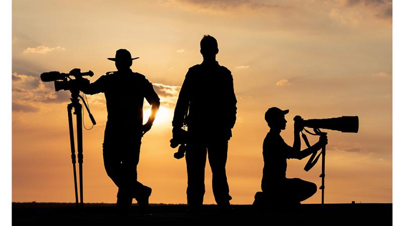 Three men with camera gear silhouetted by the sun.  