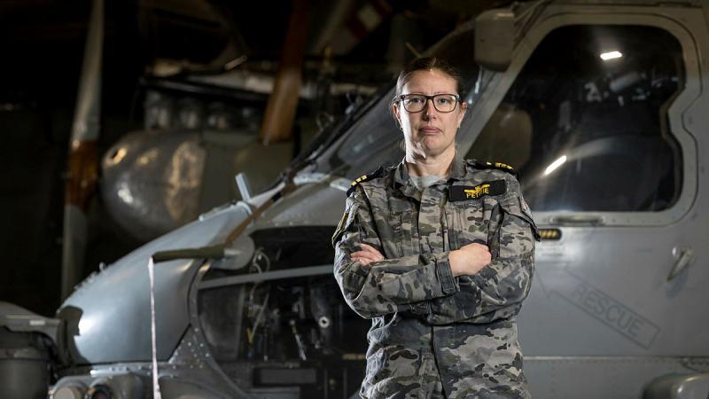 A Navy member stand with her arms crossed in front of an aircraft inside a storage annex..