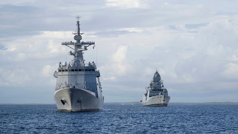 Two ships, one closer to camera than the other, sit on calm seas on a cloudy day.