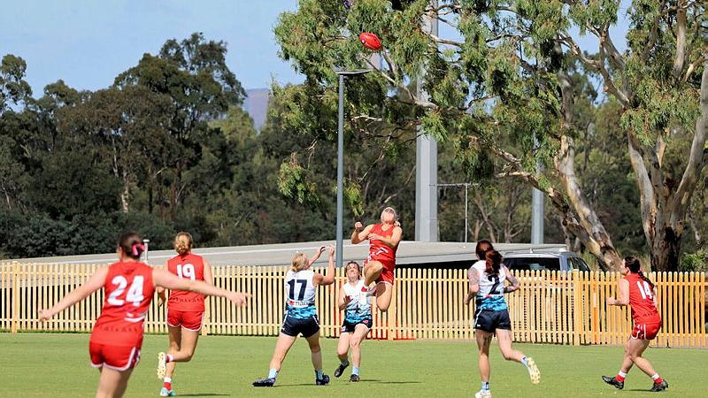 A female AFL player jumps up to a high ball with other players running towards her.