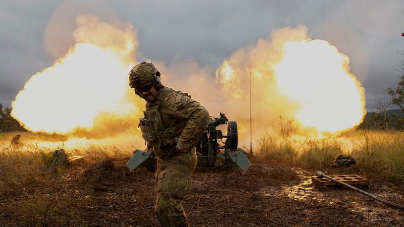 A soldier stands in the foreground of an explosion behind him. Two balls of fire are seen.